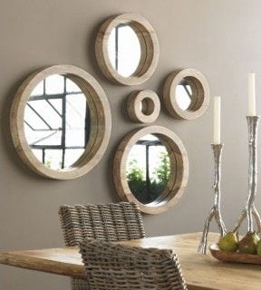 32 Mirror Decorating Ideas - Transform Home With Mirrors 11 Five circular decorative mirrors in light wood frames are staggered on a neutral wall above a rustic wooden dining table.
