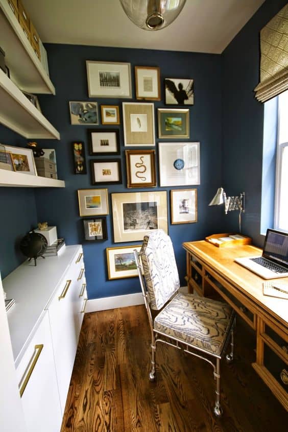 Cozy home office with a wooden desk against a blue wall, elegant metal chair, and gallery wall. Floating shelves maximize storage and light.