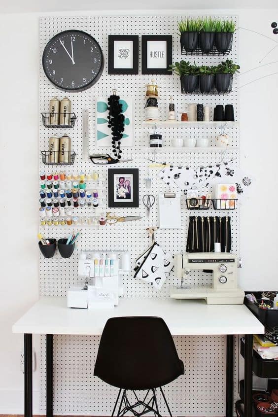 Craft room featuring a pegboard wall for organized storage, colorful spools, a sewing machine on a spacious desk, and potted plants.