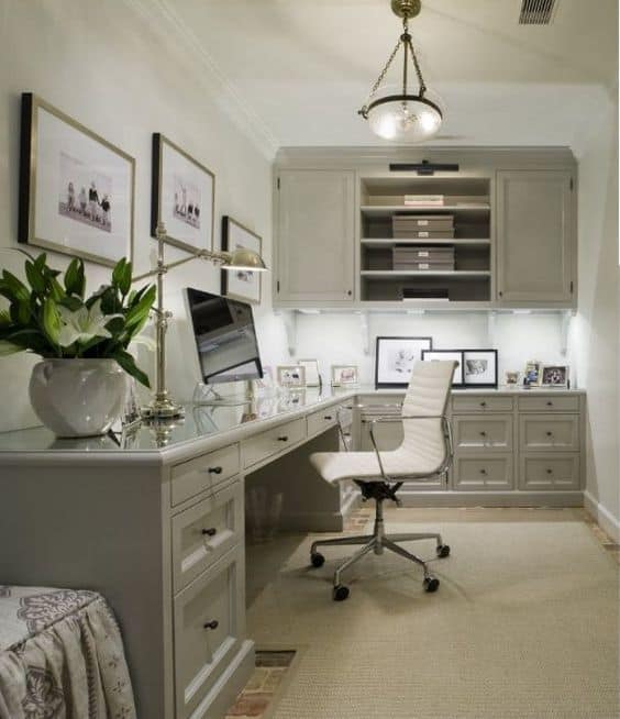 Sleek light gray built-in desk in a small home office, featuring storage drawers and shelves, ergonomic chair, and framed prints for decor.