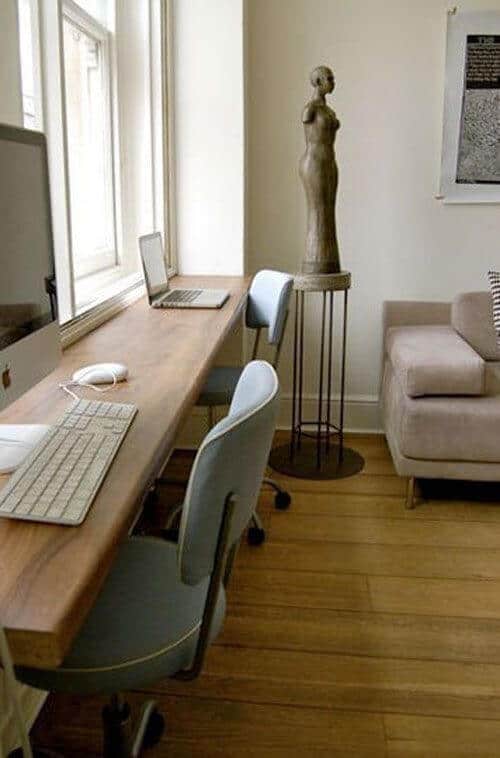 Home office features a natural wood tabletop for two laptops, stylish blue chairs, and a cozy sofa, blending productivity with chic design.