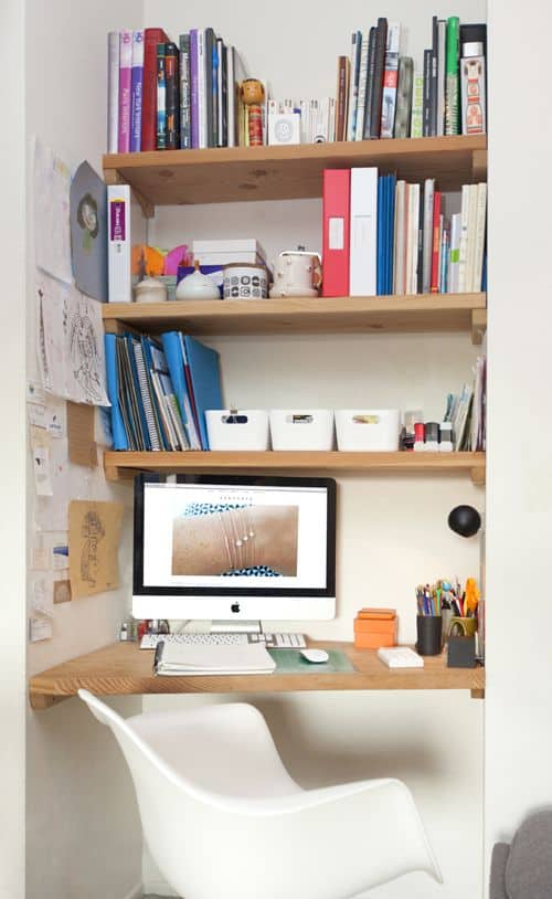 Compact home office with an L-shaped wooden desk, ergonomic chair, and three open shelves for organized storage, maximizing productivity in small spaces.