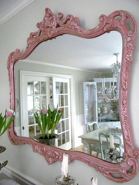32 Mirror Decorating Ideas - Transform Home With Mirrors 18 Ornate pink decorative mirror with intricate detailing, reflecting light on a gray wall, paired with a simple console table and greenery.