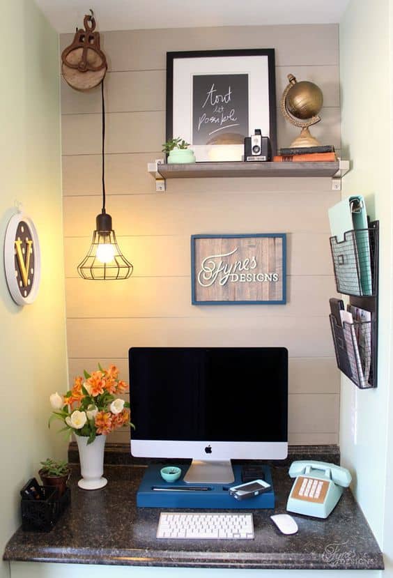 Compact home office featuring a dark granite desk, an all-in-one computer, vintage phone, and decorative shelves, all in a calming pastel setting.