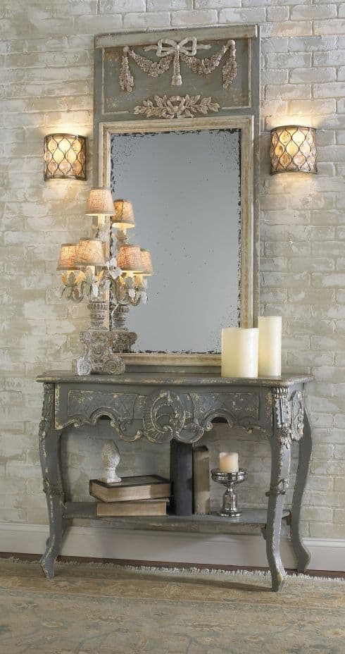 32 Mirror Decorating Ideas - Transform Home With Mirrors 19 A vintage-style mirror with decorative elements hangs above a console table, enhancing a stylish entry area with warm lighting.