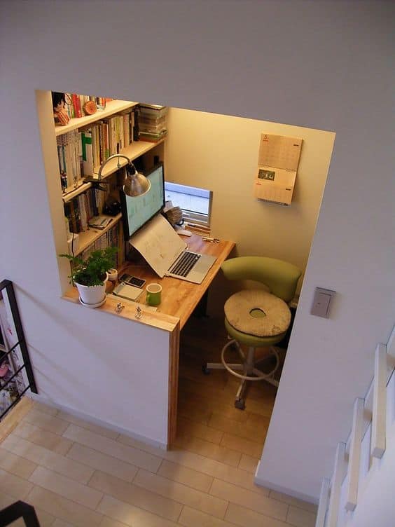 Home office setup with a mounted wooden desk, compact stool, and wall-mounted bookshelf, optimized for small spaces and productivity.
