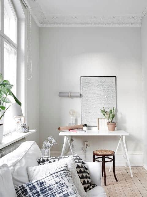 Bright living room office combo with light gray walls, large window, white desk, natural wood chair, and decorative plants.