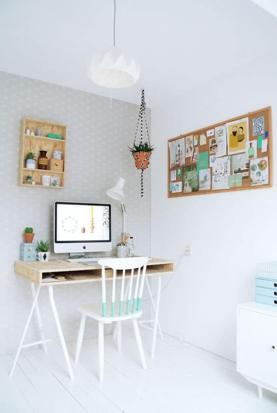 Minimalist home office with a light wooden desk, white chair, and green accent. Corkboard displays notes; potted plants enhance the serene space.