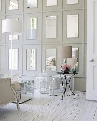 32 Mirror Decorating Ideas - Transform Home With Mirrors 23 Modern living room with a white paneled wall and rectangular mirrors, creating a spacious feel. Features a light sofa, round table, and decorative birdcages.