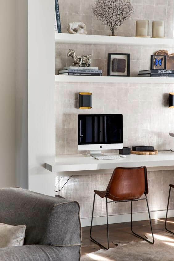 Home office features a white desk against a textured wall, complemented by shelving, a sleek computer setup, and a cozy sectional.