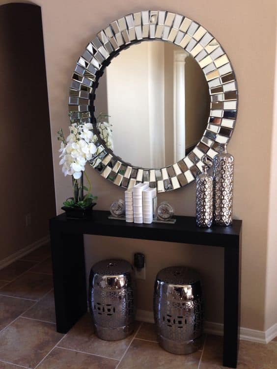 32 Mirror Decorating Ideas - Transform Home With Mirrors 25 Round mirror centerpiece on a black console table, accented by metallic stools, vases, and orchids, enhancing entryway decor.