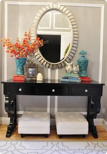 32 Mirror Decorating Ideas - Transform Home With Mirrors 26 Sleek black console table with ornate legs, topped by a sunburst mirror, flanked by plush white ottomans against a light gray wall.