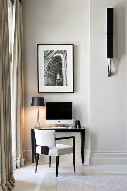 Sleek black desk with computer in a living room office combo, accented by a modern white chair and stylish table lamp, framed by sheer curtains.