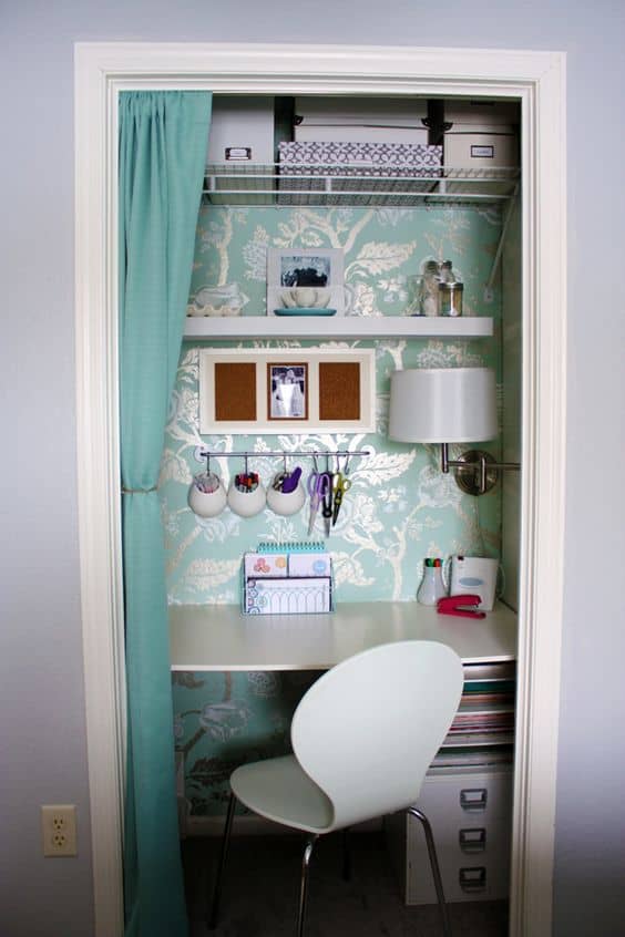Home office within a closet, featuring a white table, curved chair, teal floral wallpaper, open shelves, and organized storage solutions.