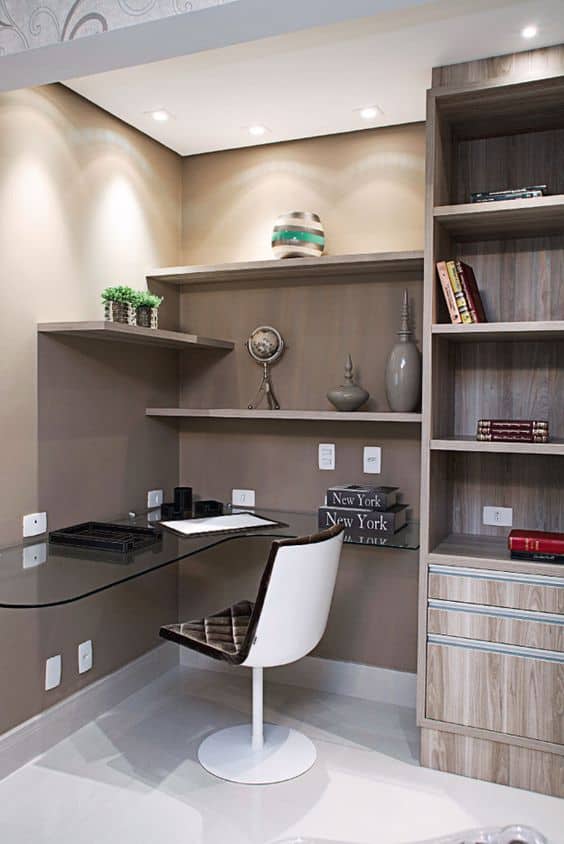 Compact home office with a glass desk, minimalist white chair, and floating wooden shelves. Neutral tones and LED lighting enhance the modern design.