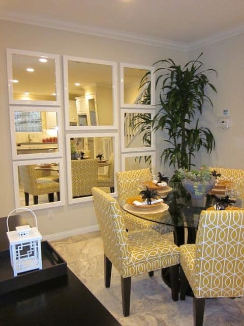 32 Mirror Decorating Ideas - Transform Home With Mirrors 2 Vibrant dining area with a round glass table, upholstered chairs, and four square mirrors enhancing light and depth. Modern decor and plants.