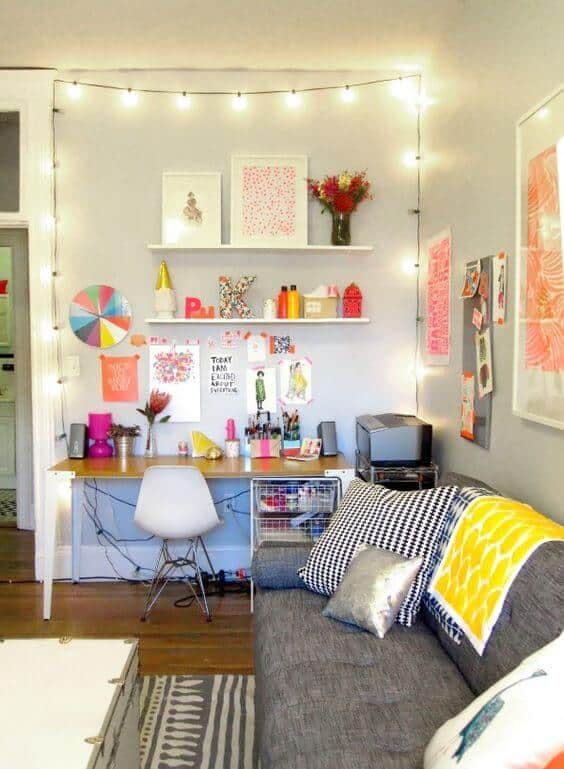 Compact workspace in a bright living area features a light-toned wooden desk, sleek white chair, cozy grey sofa, and vibrant decor.