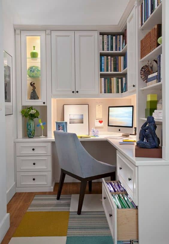 Compact home office layout with built-in cabinetry, smooth white finish, warm hardwood flooring, and vibrant area rug. Ideal for maximizing space and productivity.