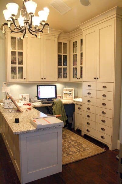 Functional home office featuring cream cabinetry, dark hardwood flooring, a granite-topped island, and tall storage cabinets for organization.