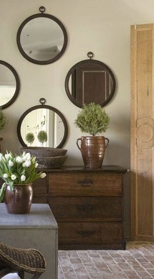 32 Mirror Decorating Ideas - Transform Home With Mirrors 8 Six circular mirrors of varying sizes layered above a vintage wooden dresser, creating a stylish living room decor with natural tones.