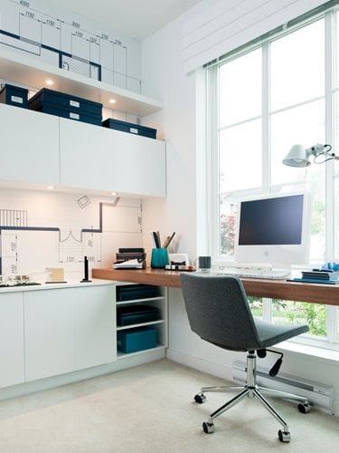 Home office with white cabinetry and a 6-foot wooden desk. Open shelving for organized storage, large window for natural light, and ergonomic chair.
