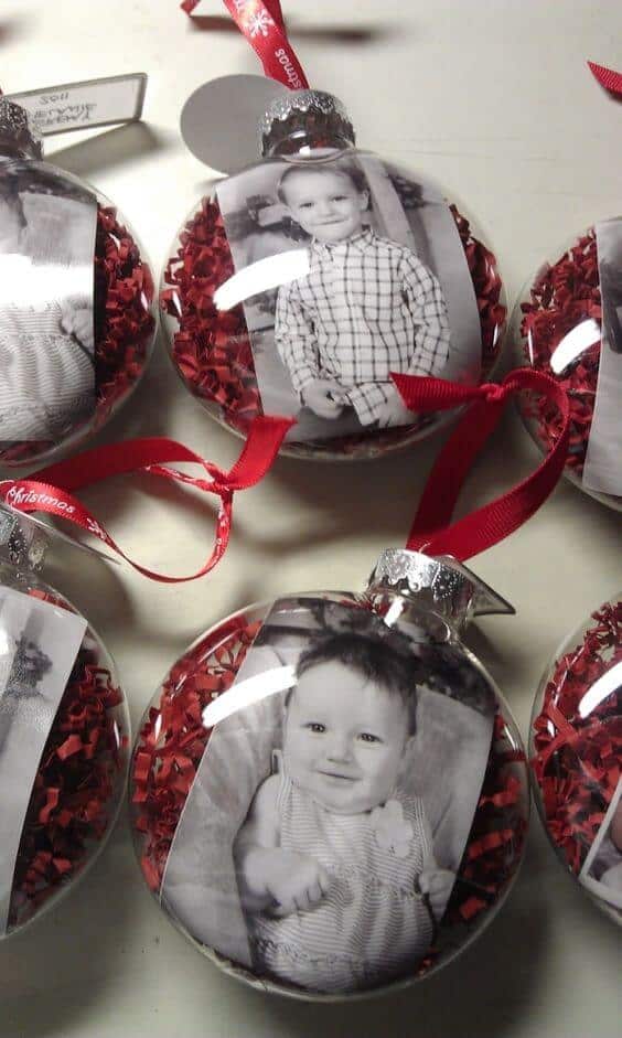 37 DIY Christmas Ornament Ideas For You Unique Decor 2 Clear spherical DIY Christmas ornaments with black-and-white photos, vibrant red shredded paper, silver caps, and red ribbons for hanging.
