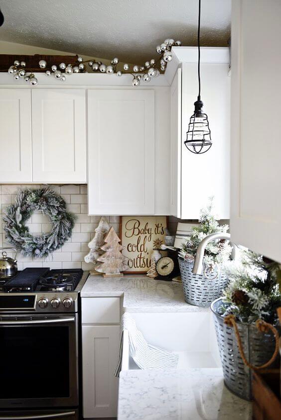 Decorative Christmas ornaments hang from a minimalist kitchen wreath, featuring seasonal accents and soft natural light, enhancing the festive atmosphere.