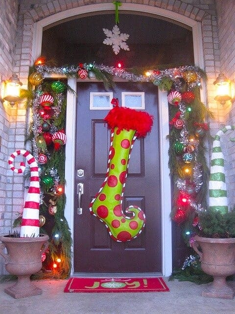 Vibrant green Christmas stocking with red polka dots hangs on a dark brown door, flanked by candy cane decorations and colorful ornaments.