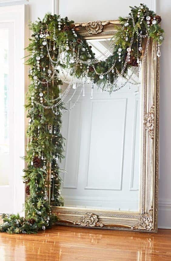 Christmas ornaments elegantly framed by a large gold mirror, adorned with evergreen garlands, silver beads, and festive decorations.