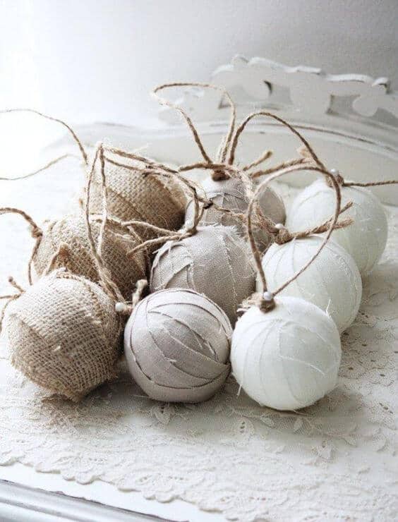 37 DIY Christmas Ornament Ideas For You Unique Decor 27 Decorative balls in neutral tones are clustered together, featuring burlap and linen textures. Some are adorned with twine for a rustic touch, placed on lace fabric.