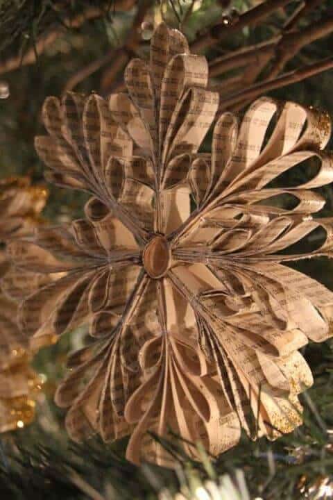 37 DIY Christmas Ornament Ideas For You Unique Decor 30 Delicate paper snowflake ornaments crafted from vintage book pages, featuring a six-petal design in muted cream and brown, hanging on a pine tree.