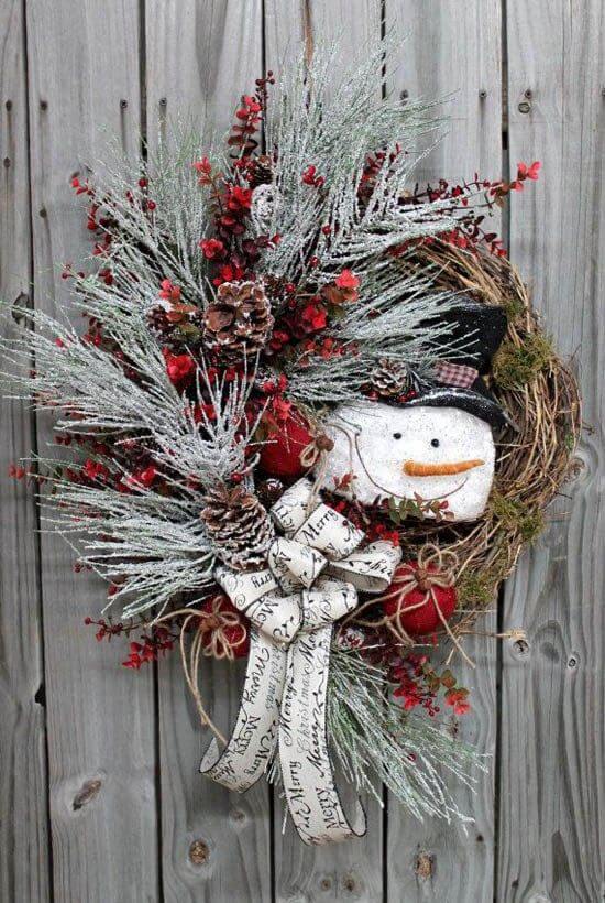 A festive Christmas wreath featuring a snowman centerpiece, adorned with evergreen foliage, berries, and pine cones, perfect for holiday decor.