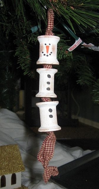 37 DIY Christmas Ornament Ideas For You Unique Decor 35 Three stacked white wooden spools resembling a snowman, with hand-painted features and buttons, hang from a checkered ribbon. Perfect for DIY Christmas ornaments.