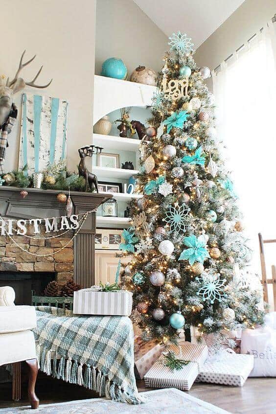 A seven-foot evergreen tree adorned with turquoise and gold ornaments, silver snowflakes, and white tinsel, surrounded by gifts in a cozy living room.