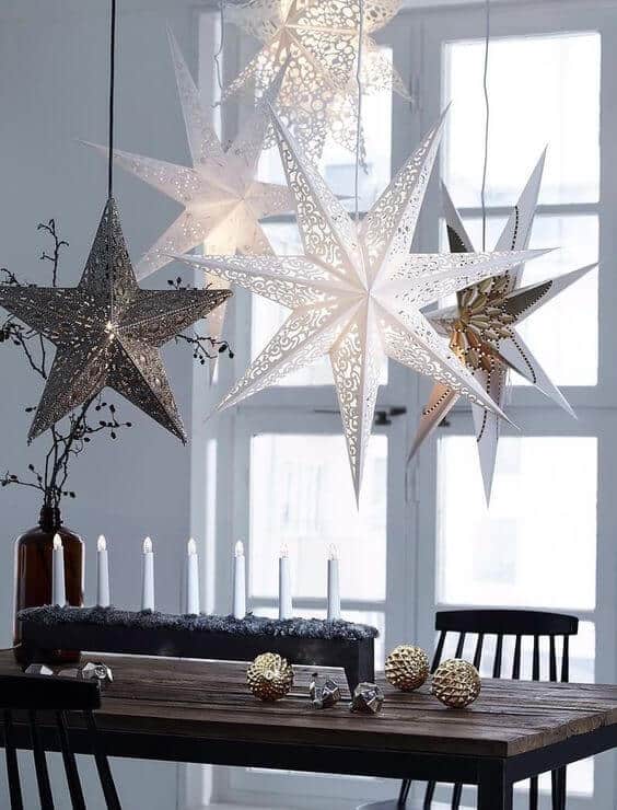 Star-shaped hanging lights illuminate a dining area with a dark-stained wooden table, gold accents, and white candles, enhancing the festive ambiance.