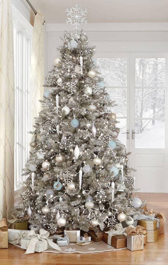 Christmas tree adorned with silver and light blue glass ornaments, surrounded by wrapped presents, set against a snowy backdrop.