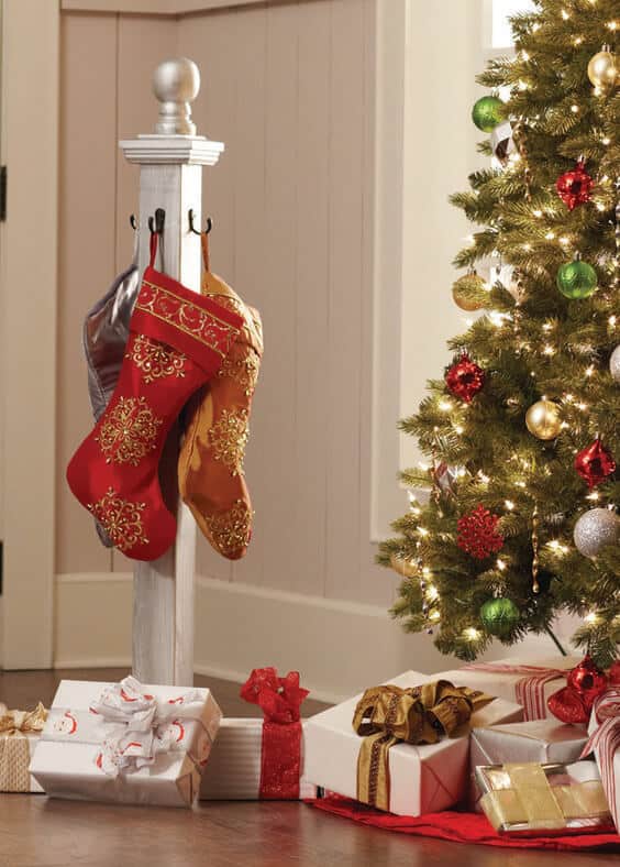 A cozy corner features an evergreen tree adorned with colorful Christmas ornaments, twinkling lights, and ornate red and gold stockings.