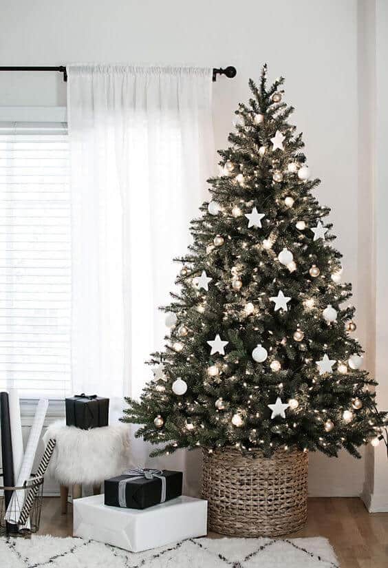 Christmas tree adorned with white ornaments and warm lights, surrounded by neatly wrapped gifts on a textured rug, creating a cozy holiday vibe.