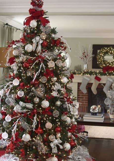 Christmas tree adorned with red, silver, and white ornaments, sparkling lights, and decorative ribbons, set in a cozy living room.