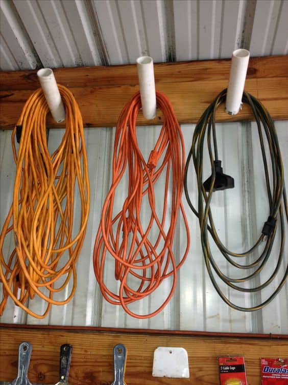 Three organized extension cords in vibrant orange and olive green, mounted on a wooden board against a metal wall, ensuring efficient cable management.