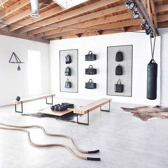 36 Home Gym Ideas - Layouts For Your Perfect Workout Spot 3 Home gym with high wooden ceilings, polished concrete floor, central wooden bench, wall-mounted storage for workout bags, and a heavy punching bag.