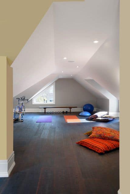 36 Home Gym Ideas - Layouts For Your Perfect Workout Spot 25 Spacious home gym with sloped ceiling, dark hardwood floor, blue exercise ball, colorful yoga mats, and bright cushions for comfort.