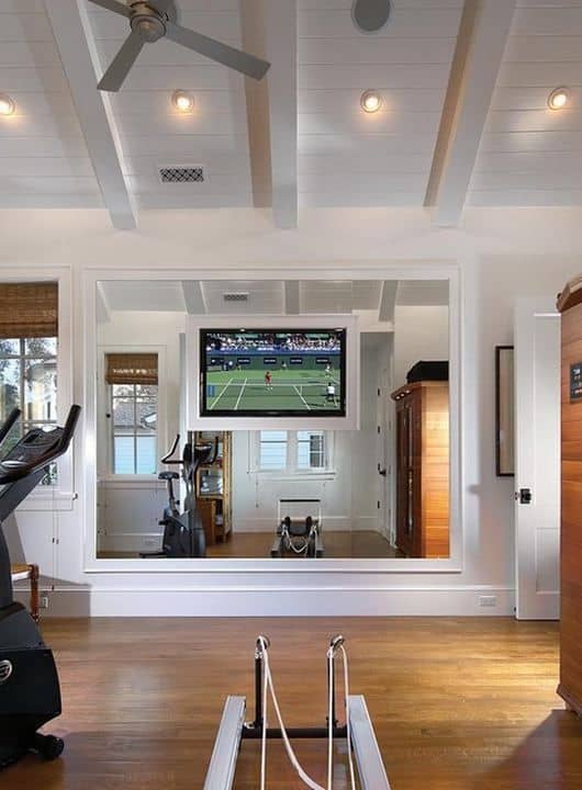 36 Home Gym Ideas - Layouts For Your Perfect Workout Spot 27 Home gym featuring a mirrored wall, flat-screen TV, treadmill, and airy ambiance with natural light, perfect for workout inspiration.