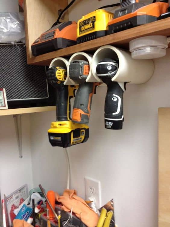 PVC pipe holders mounted on the wall store power drills vertically, color-coded for easy access. Charging stations above maintain organization.