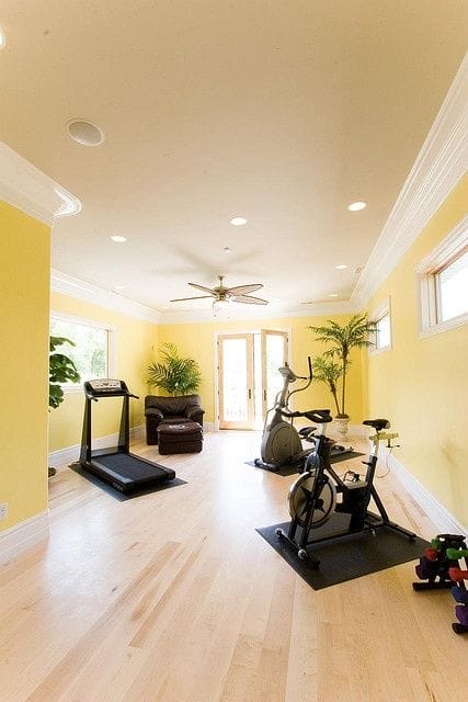 36 Home Gym Ideas - Layouts For Your Perfect Workout Spot 33 Home gym with light yellow walls, treadmill, and elliptical on rubber mats. Bright, airy space with large windows and potted plants.