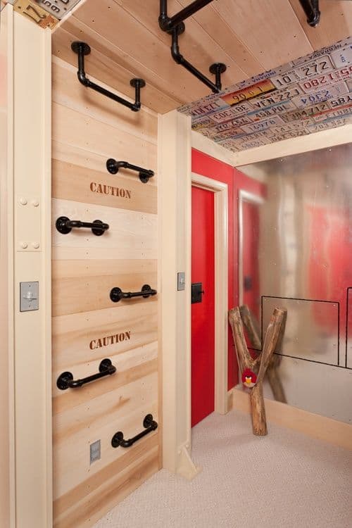 36 Home Gym Ideas - Layouts For Your Perfect Workout Spot 36 Home gym featuring a climbing wall with wooden panels and black grips, vibrant red door, and vintage license plates for decor.