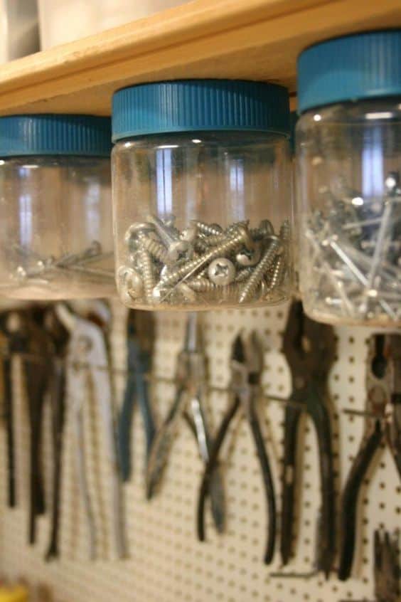 Transparent jars with blue lids hold assorted screws on a wooden shelf, optimizing vertical space. A pegboard displays neatly arranged tools.