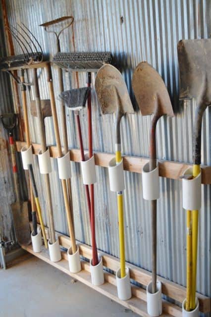 Vertical wooden panel with cylindrical holders for gardening tools like shovels and rakes, promoting organized garage storage solutions.