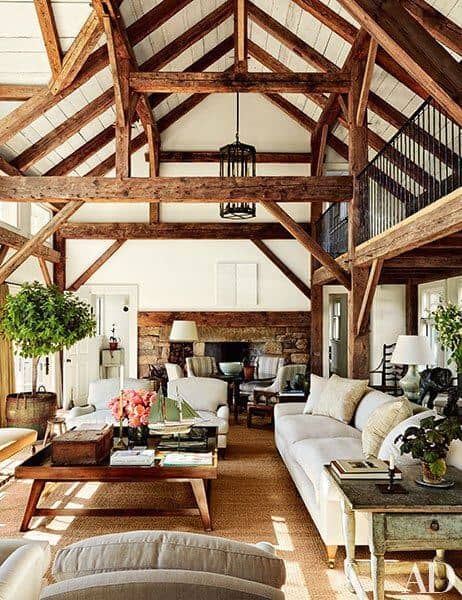 Rustic living room with exposed wooden beams, high vaulted ceiling, light-colored sectional sofa, and cozy seating area, enhanced by natural light.