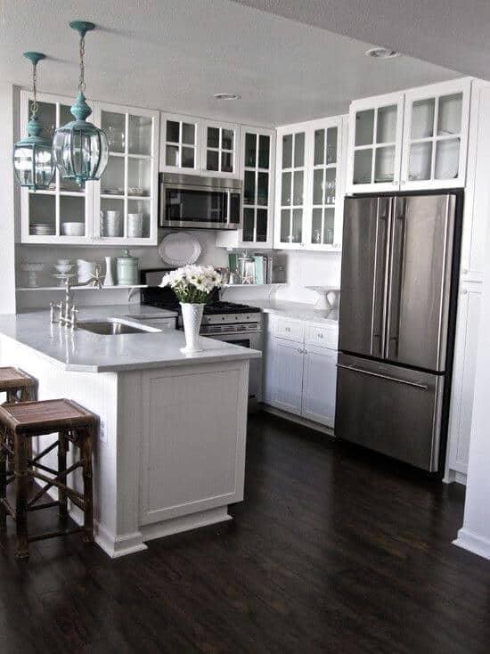 Modern small kitchen with white cabinetry, glass-front upper cabinets, a central island with marble countertop, and teal pendant lighting.